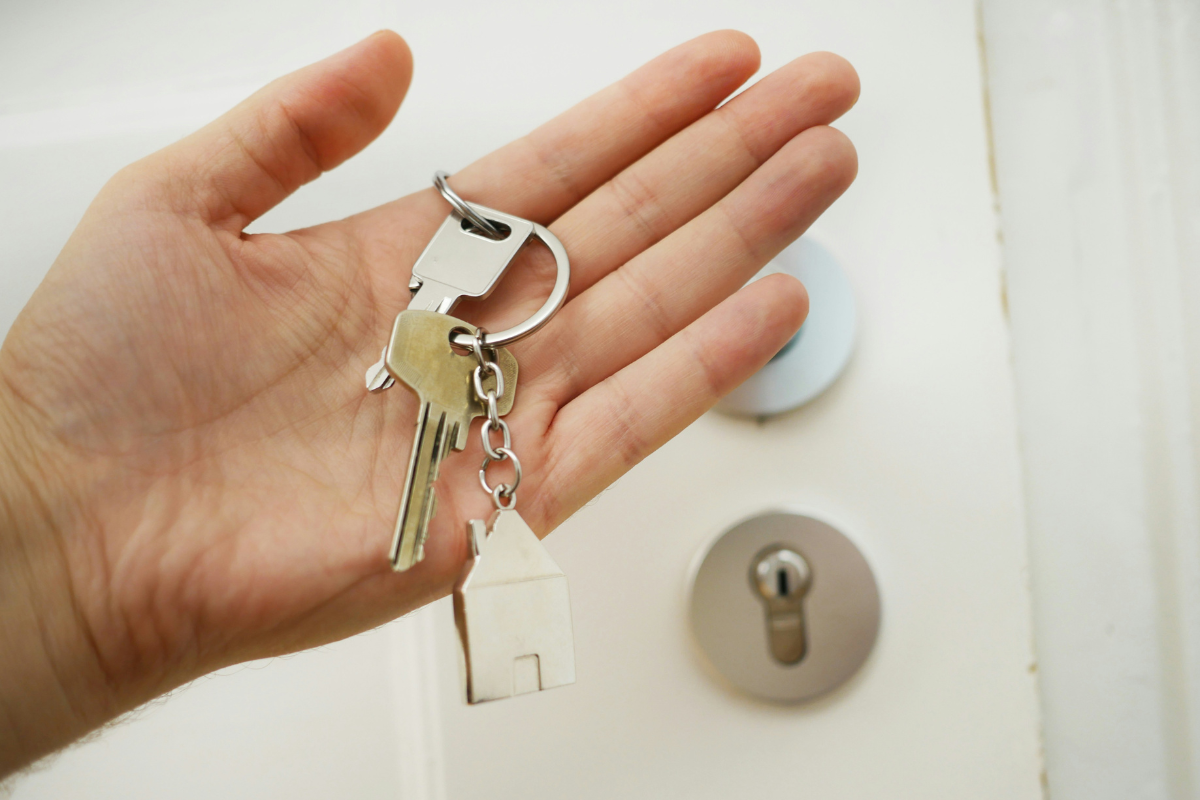 A white hand holds a set of keys in front of the lock of a door.